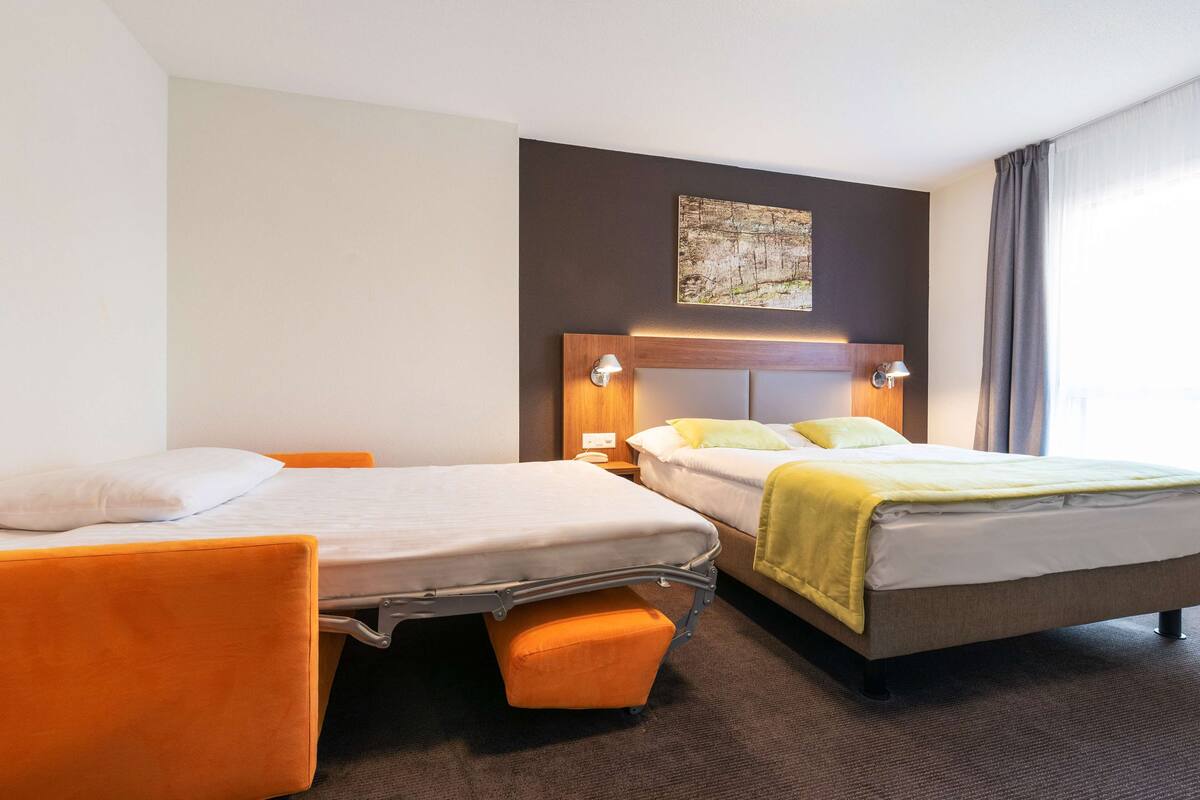 A hotel room with two beds, a small table, and a nightstand.