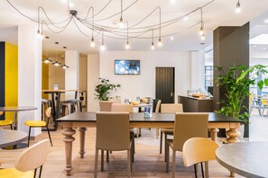 A modern dining area with multiple tables and chairs, a television mounted on the wall, and a large potted plant. - Campanile Martigny (Martigny)
