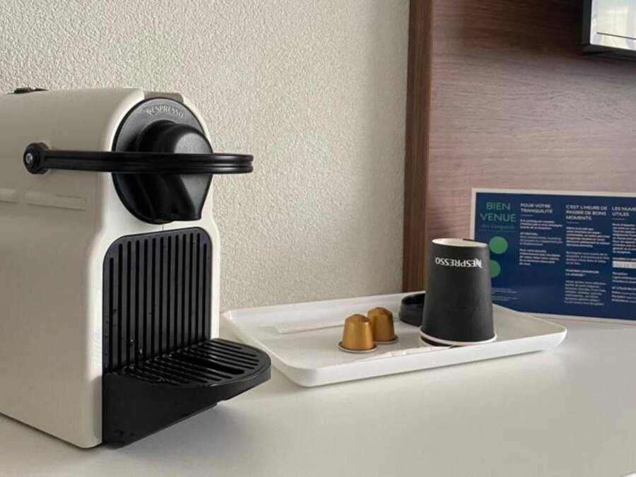 Una máquina de café Nespresso con una bandeja de cápsulas y una taza sobre una encimera de hotel.