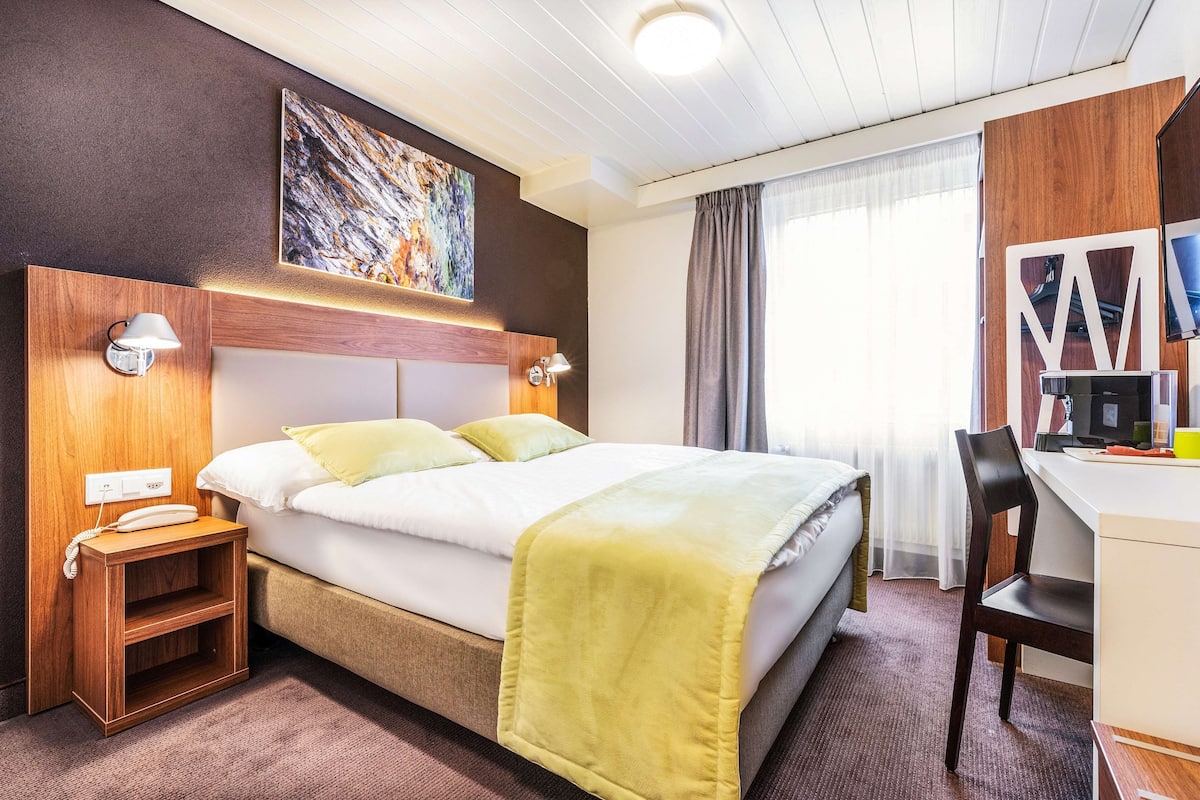 A hotel room with a bed, bedside lamps, a desk, and a chair.