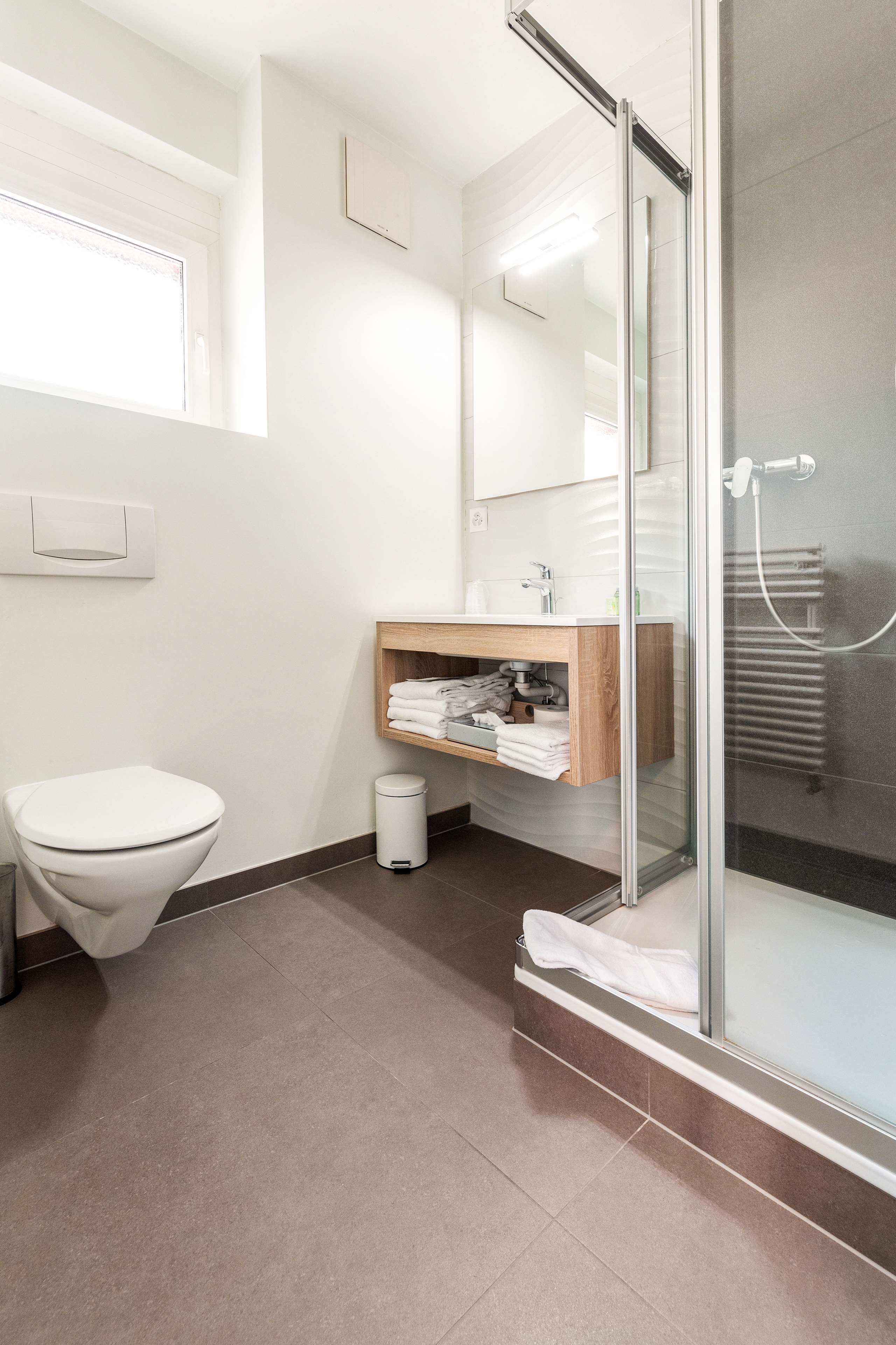 Un baño moderno con inodoro, lavamanos con tocador de madera, cabina de ducha de vidrio y barra para toallas.