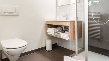Un baño moderno con inodoro, lavamanos con tocador de madera, cabina de ducha de vidrio y barra para toallas.