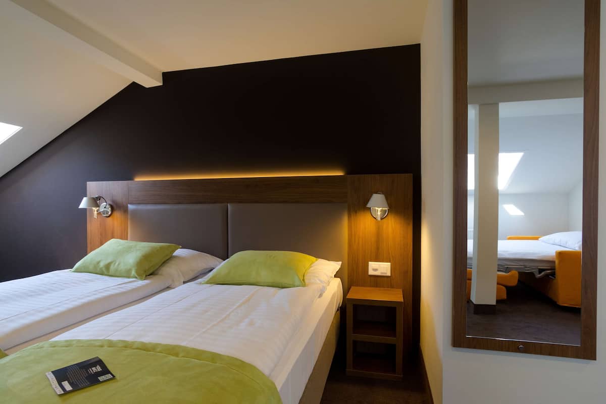 A hotel room with two beds, a small wooden nightstand, and a mirror on the wall.