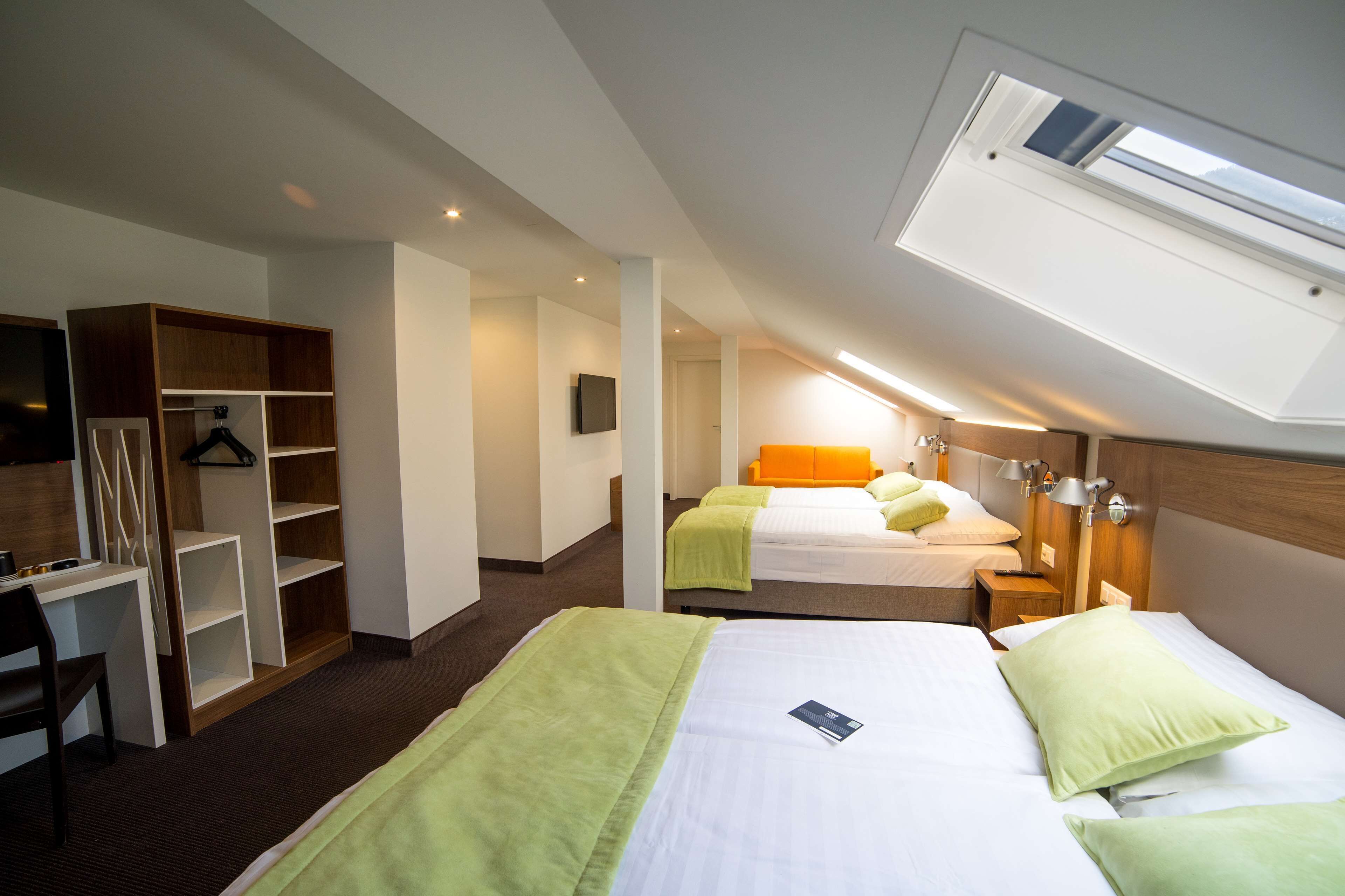 A hotel room with two beds, a desk, a wardrobe, and a skylight.