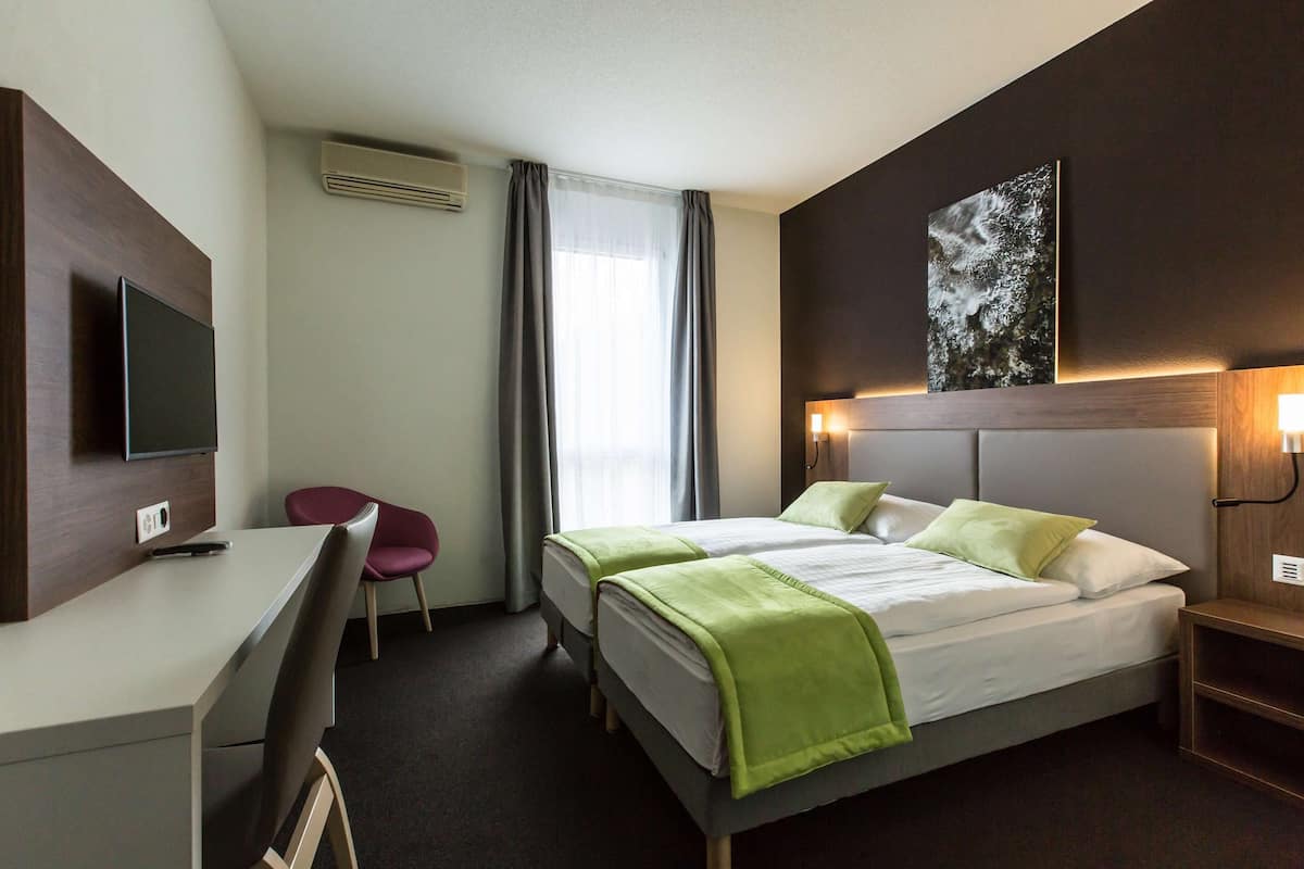 A hotel room with a bed, a desk, a chair, a TV, and a painting on the wall.
