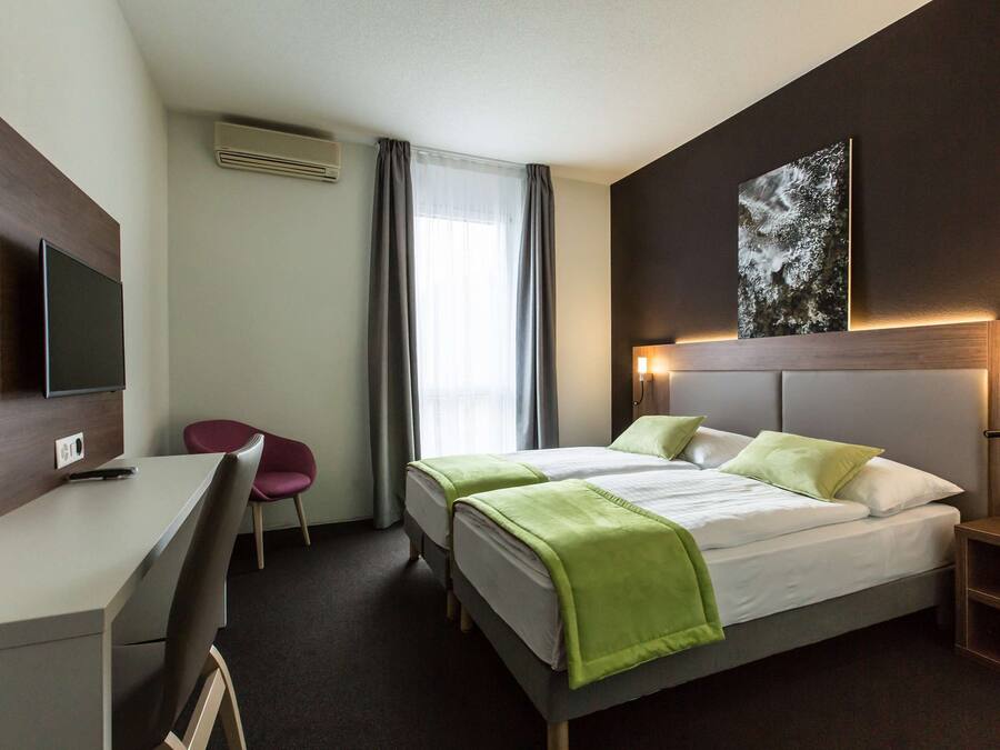 A hotel room with a bed, a desk, a chair, a TV, and a painting on the wall.