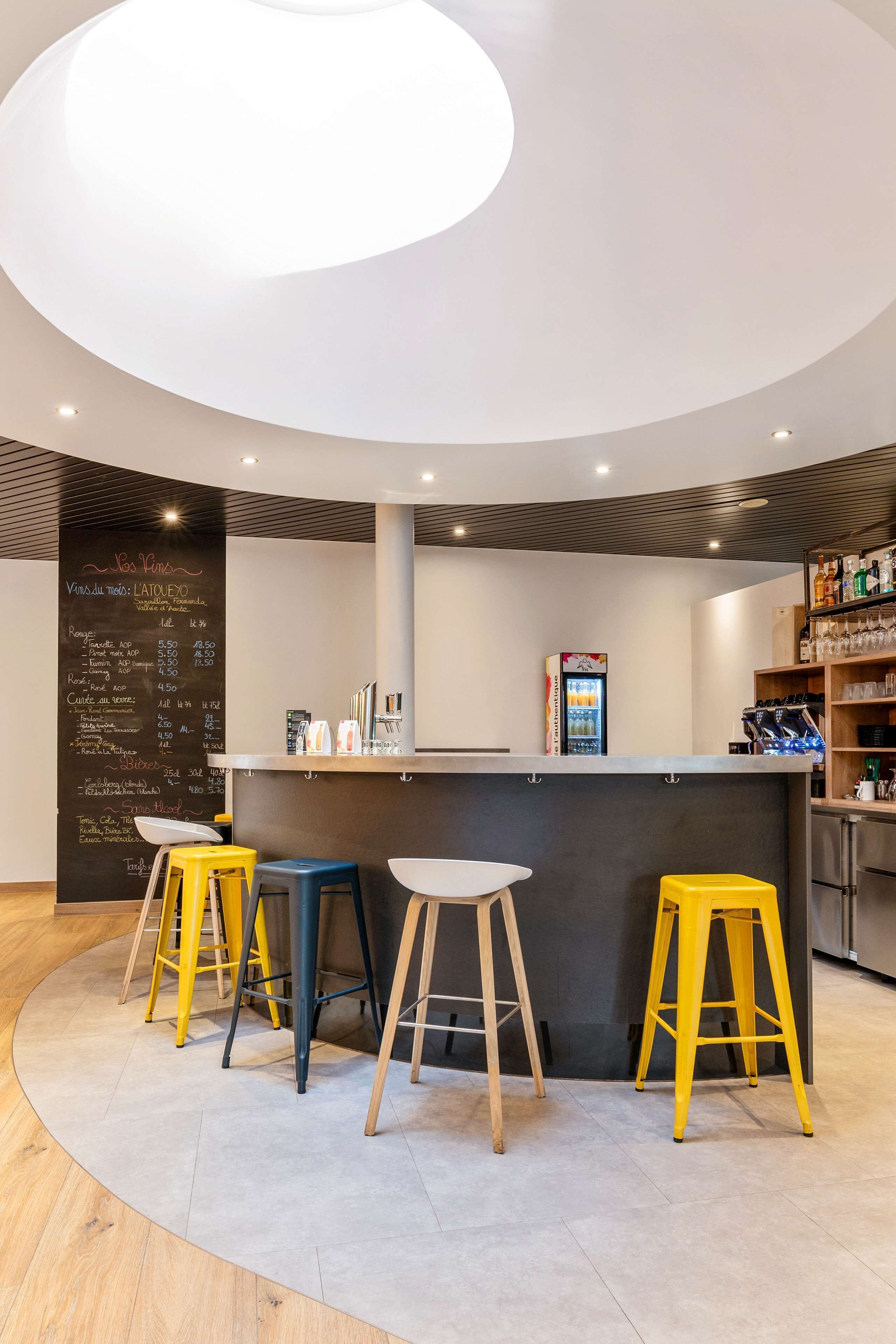 Un área de bar moderna con taburetes, una pizarra con la carta y un refrigerador.