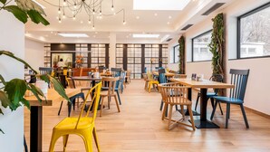 A spacious dining area with multiple tables and chairs, large windows, and a modern chandelier. - Campanile Martigny (Martigny)