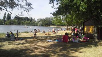 A lakeside park with people relaxing on the grass and a small wooden structure.