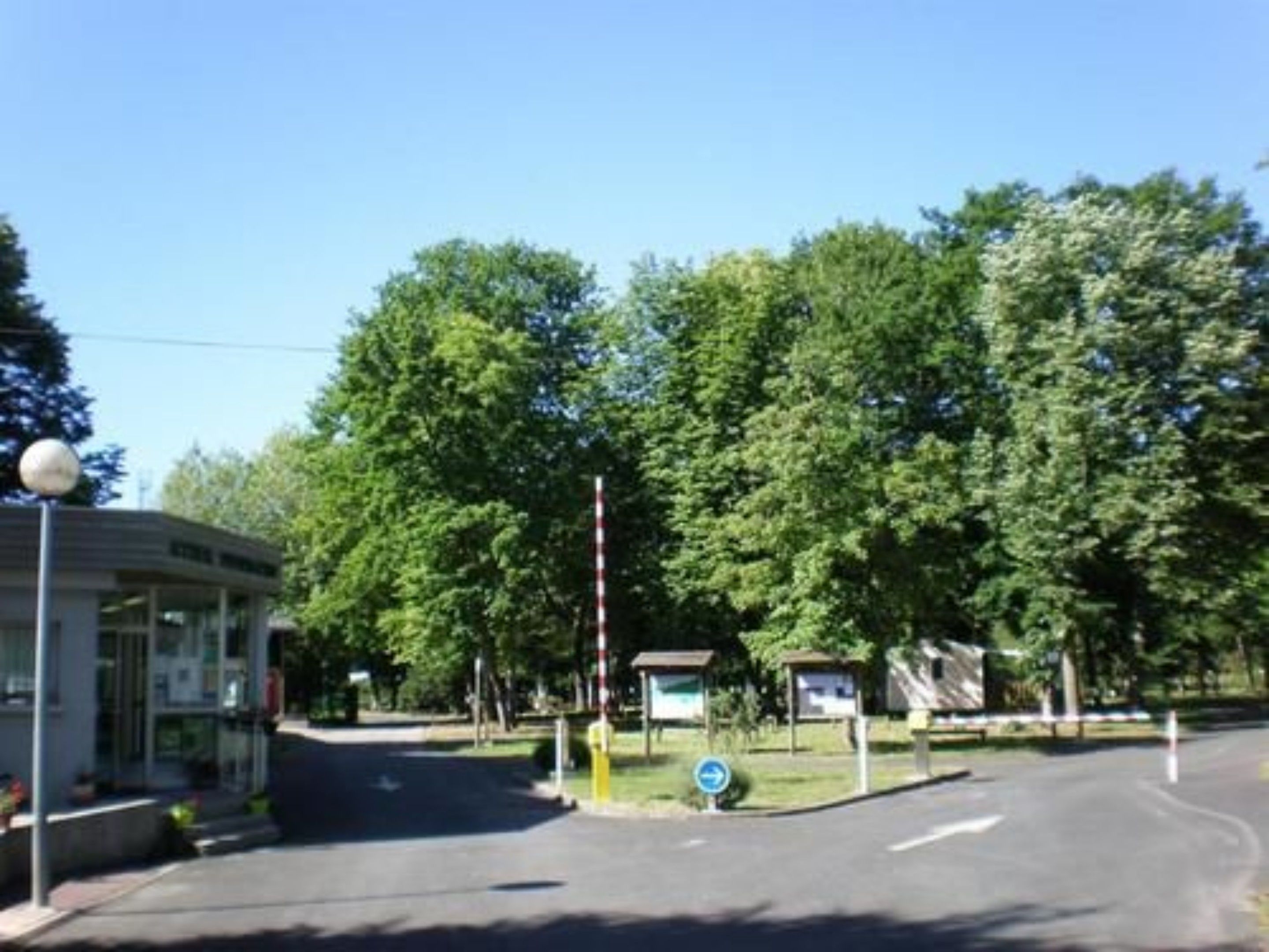 A road with a blue directional sign, a building with a signboard, and trees in the background.