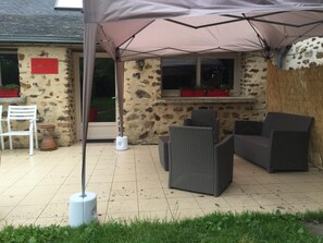 Un patio exterior con mobiliario de mimbre, un paraguas blanco y una pared de piedra.