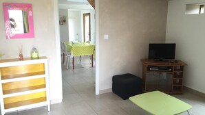 A living room with a TV, a small table, and a bench. There is a dining area in the background. - Domaine des Mille Oiseaux - Colibris (Villiers-Charlemagne)