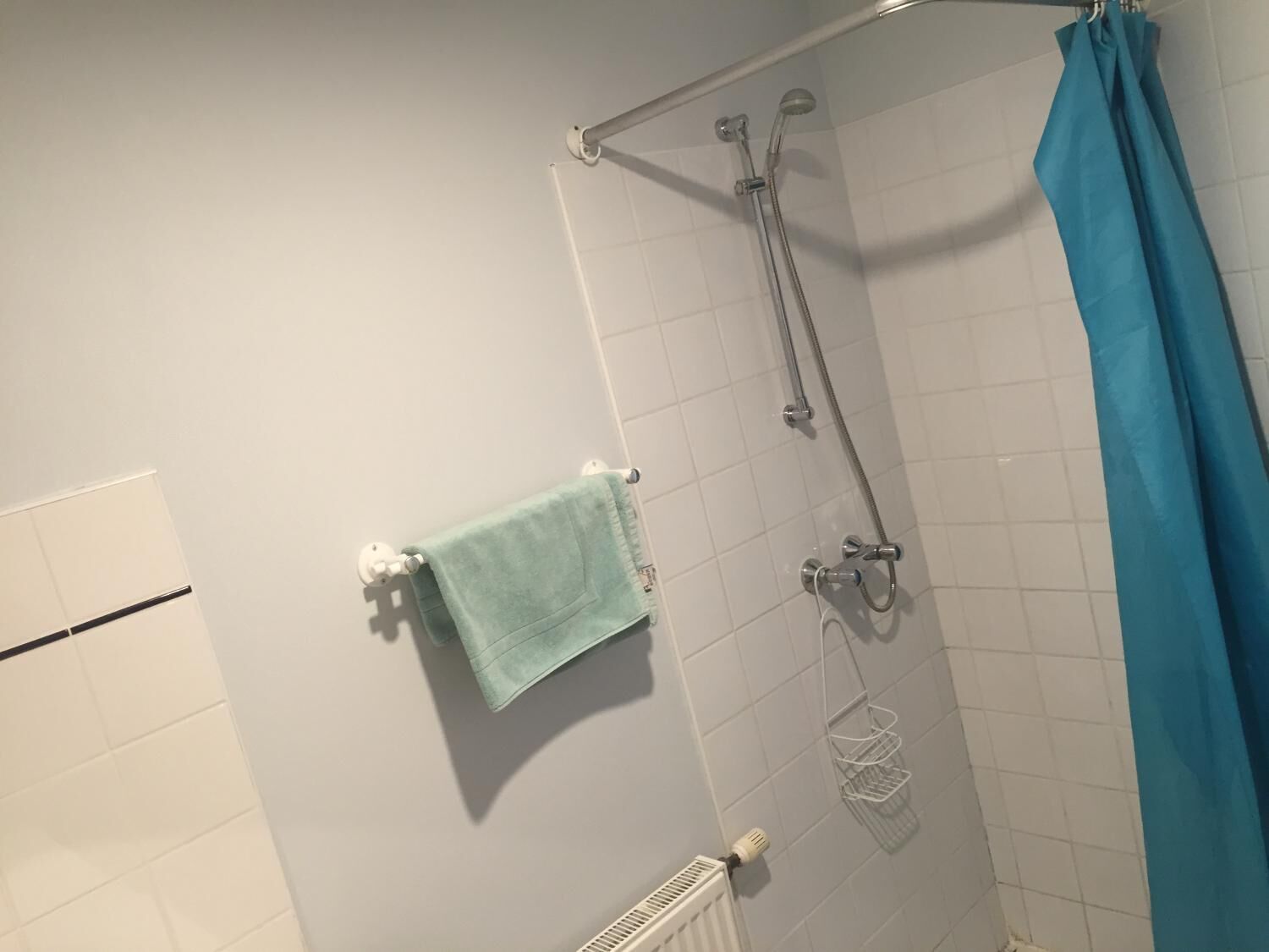 Ducha con cortina azul, toallero con una toalla azul claro y radiador blanco.