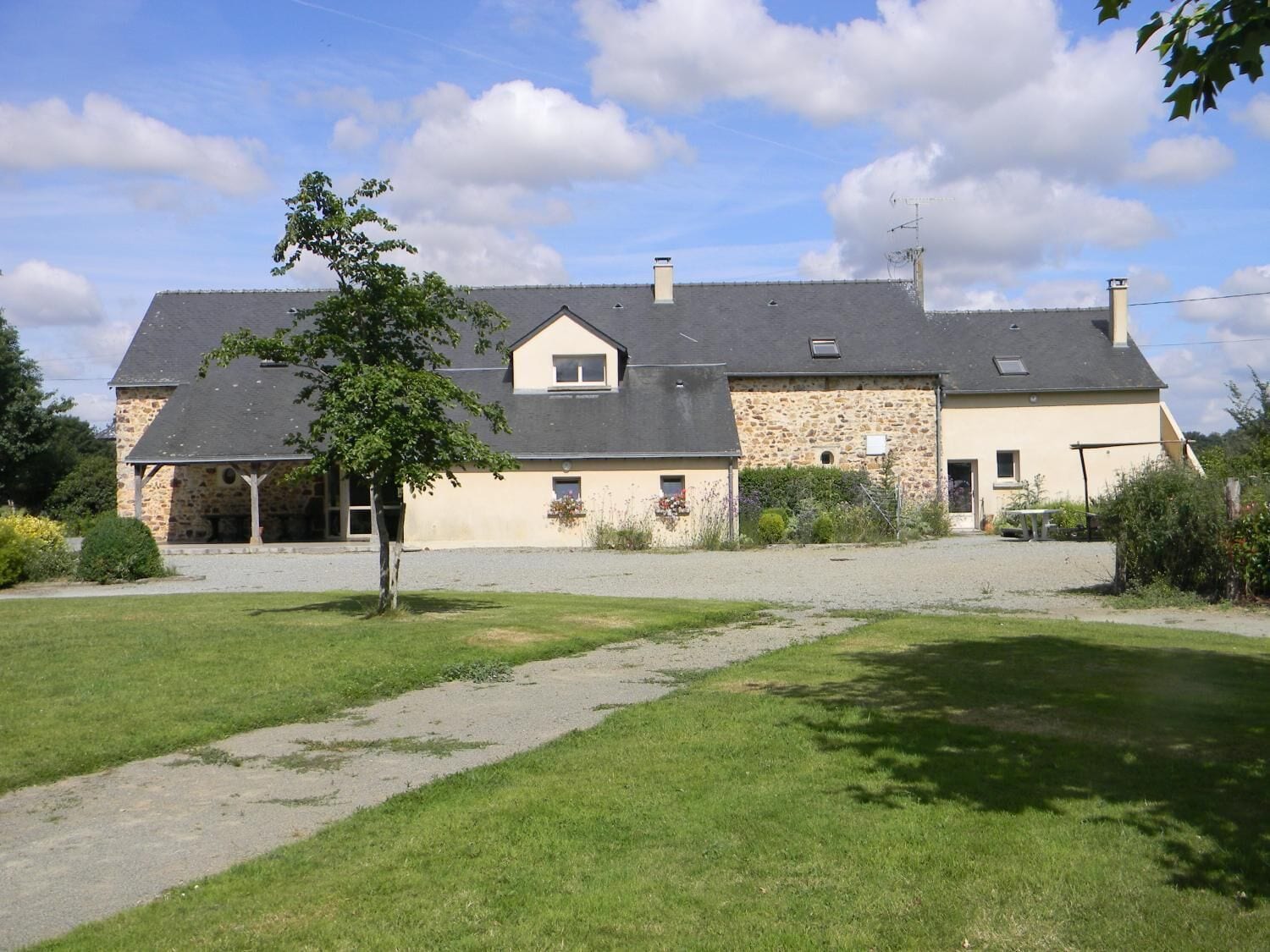 A two-story stone house with a sloped roof, a covered porch, and a gravel driveway.