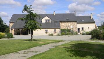 A two-story stone house with a sloped roof, a covered porch, and a gravel driveway.