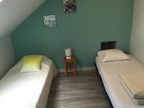 Una habitación pequeña y triangular con dos camas, una mesita de noche y una pared decorada con obras de arte.