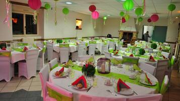 A banquet hall with round tables set for a formal event, featuring green and white tablecloths, white chairs, and hanging paper lanterns.