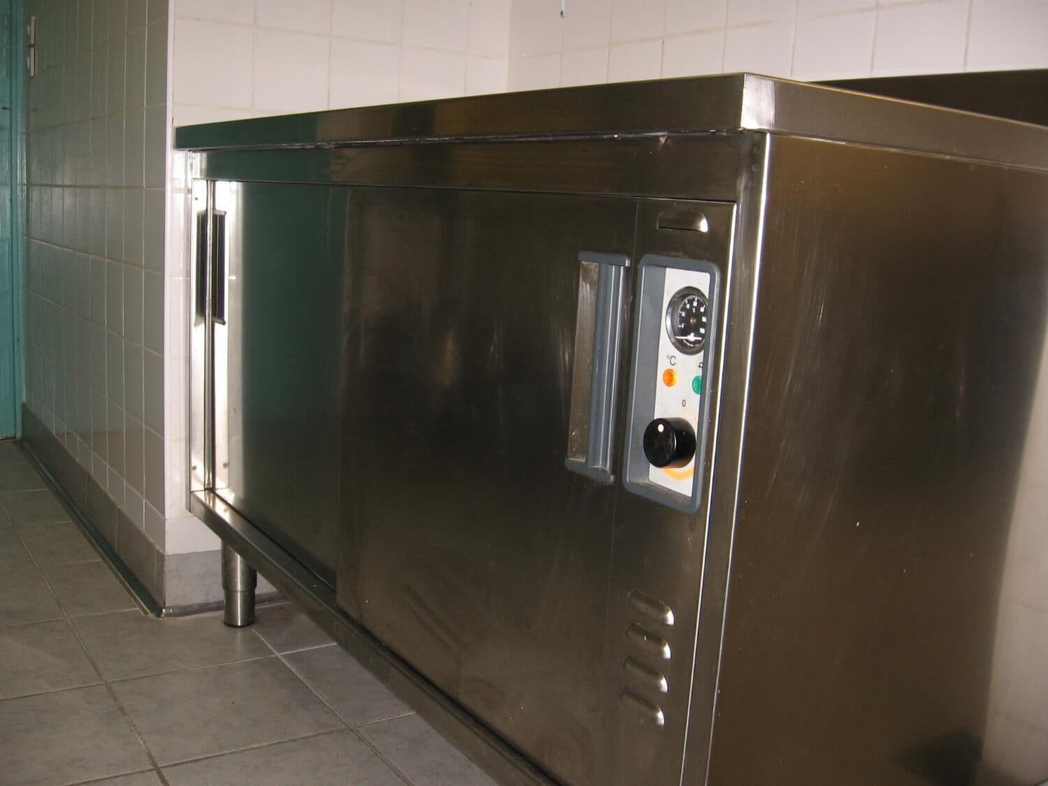 A stainless steel commercial kitchen with a control panel, a stainless steel sink, and a tiled backsplash.