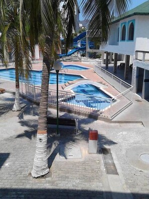 Zona de piscina con tobogán de agua, palmeras y un área de estar cubierta.