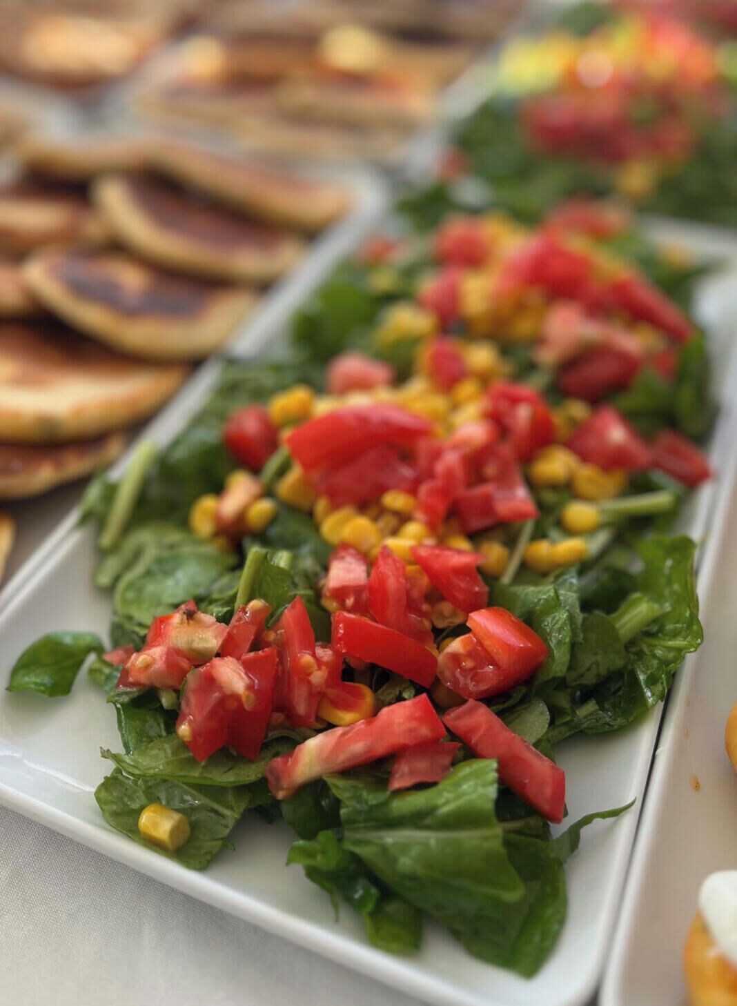 A plated salad with greens, tomatoes, and corn.