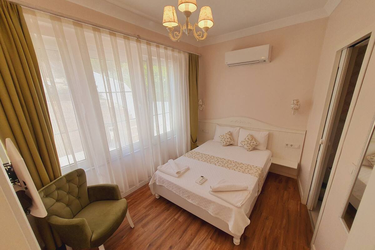 Una habitación de hotel con una cama, un sillón verde, una araña y un equipo de aire acondicionado.
