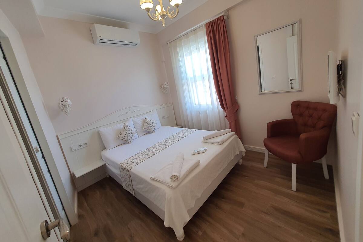 Una habitación de hotel con cama, sillón, candelabro y espejo.