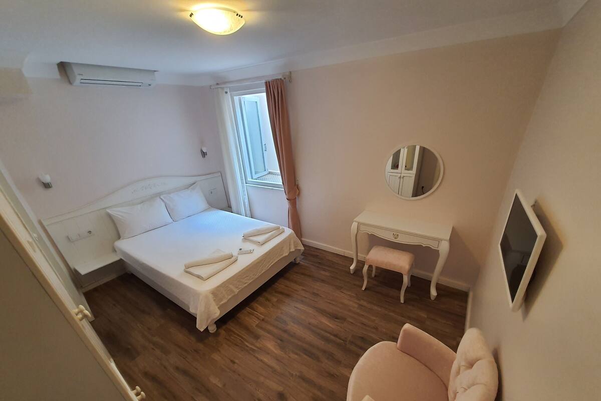 Un dormitorio con cama, escritorio, silla, espejo y televisor.