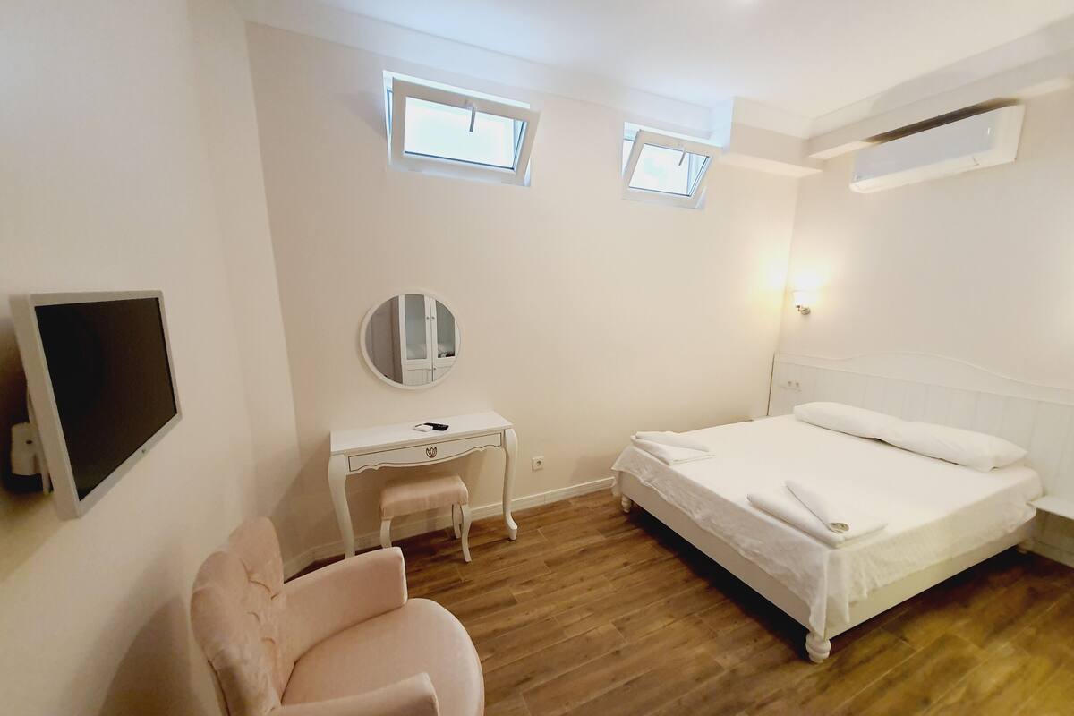 Un dormitorio con una cama, un escritorio, una silla, un televisor y dos ventanas.
