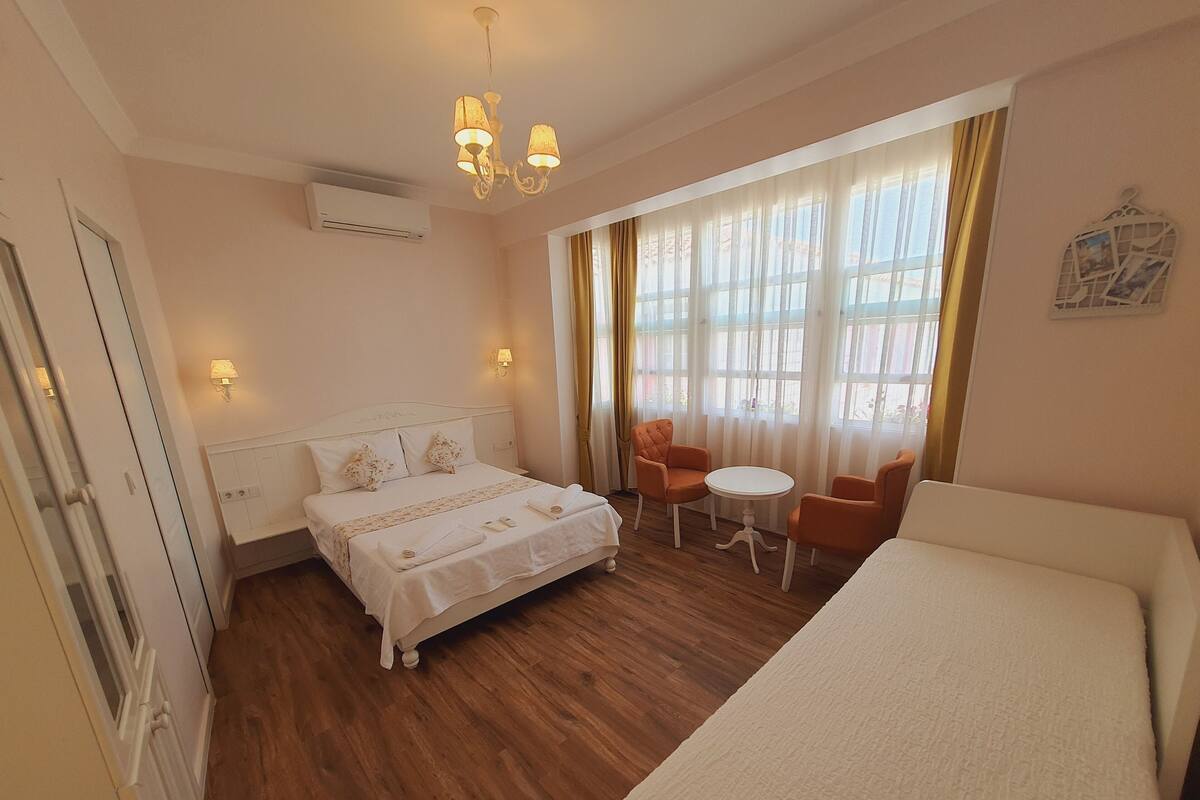 Una habitación de hotel con cama, una mesita, dos sillas y una ventana con cortinas.