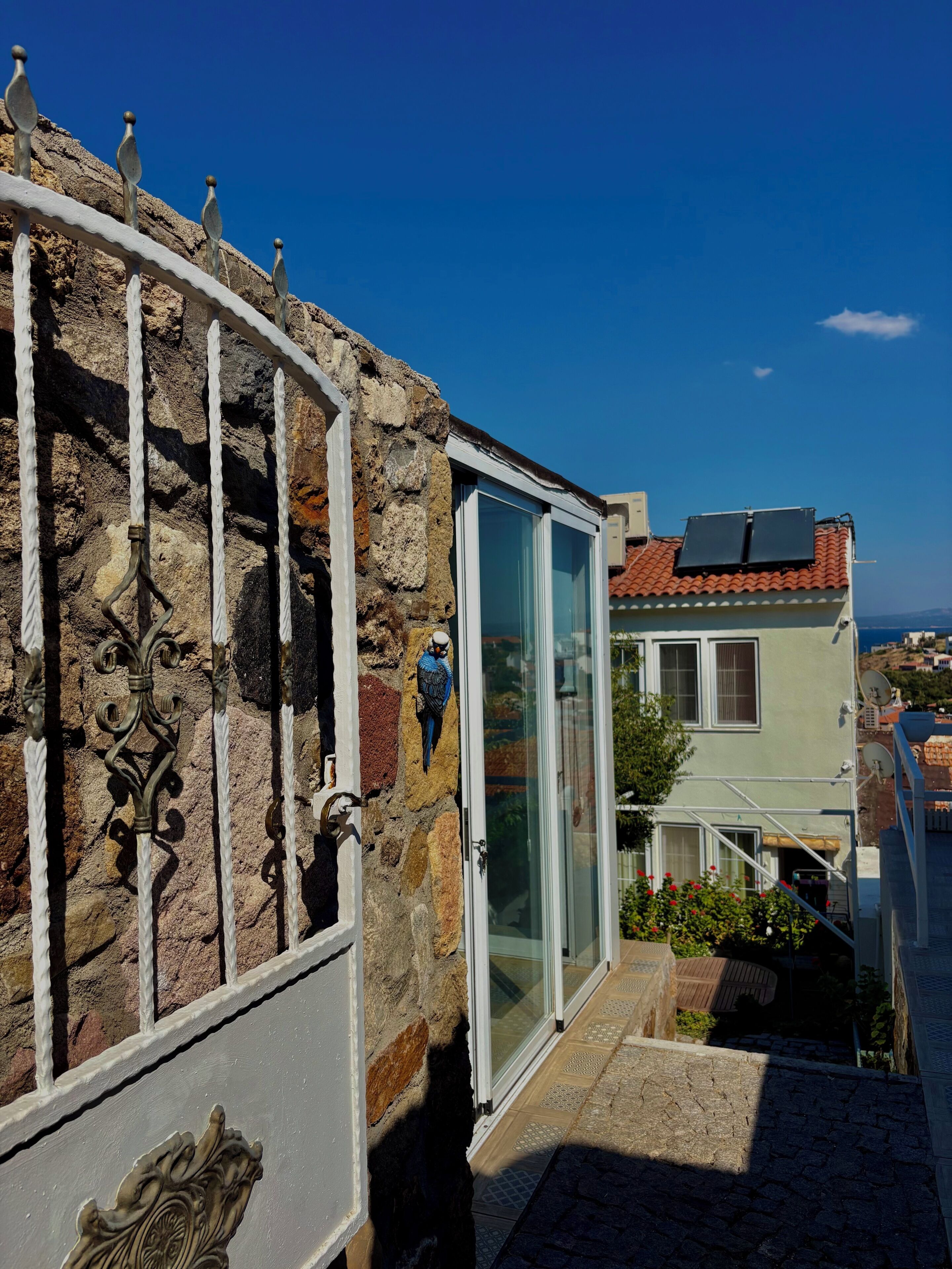 A stone wall with a metal gate, a glass door, and a view of a building with a tiled roof.