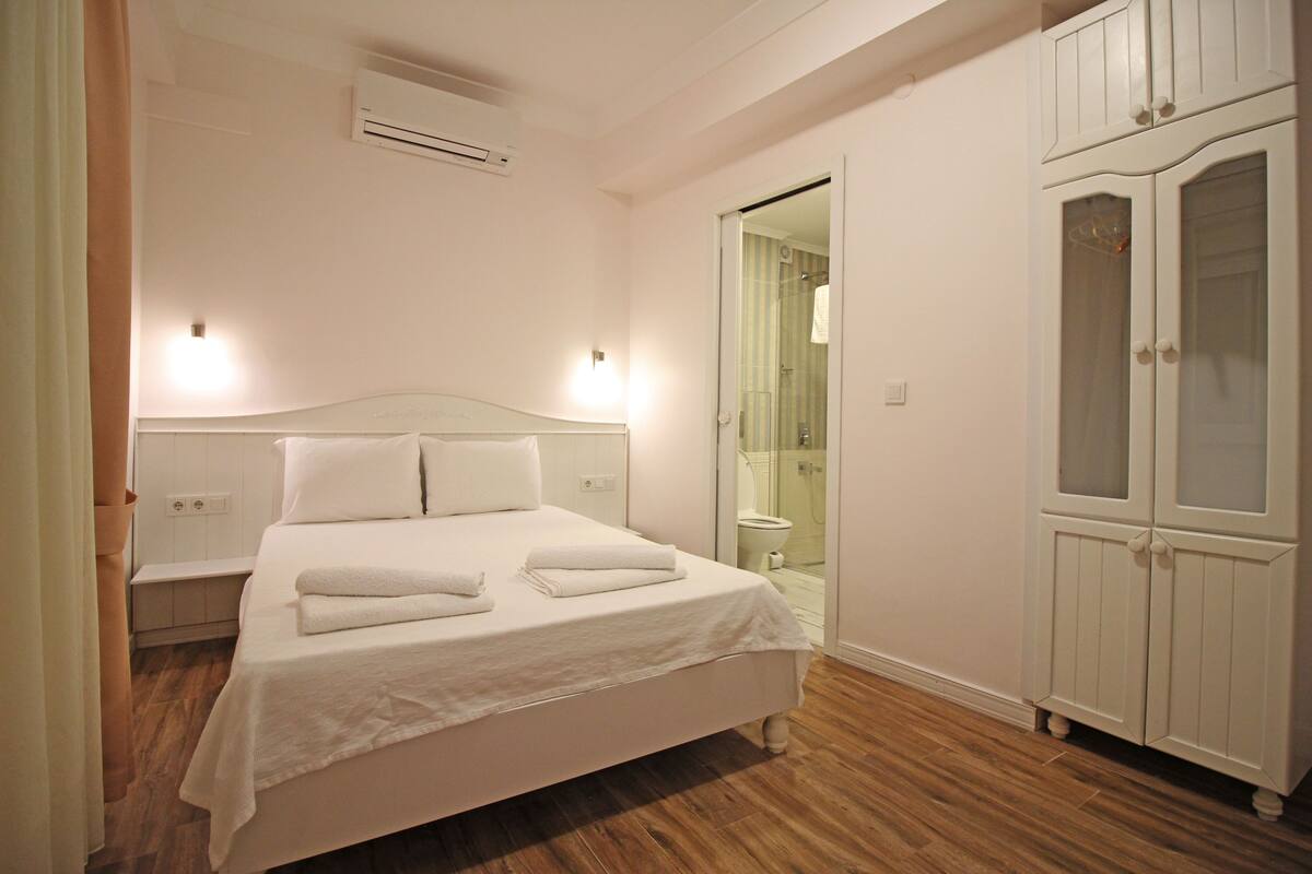 Un dormitorio con cama, mesitas de noche, aire acondicionado, armario y un baño visible a través de una puerta abierta.