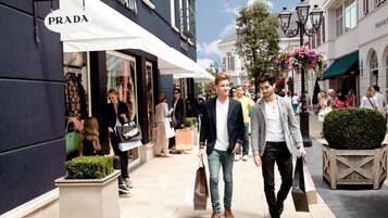 A street with a Prada store, people walking, and a flower arrangement.