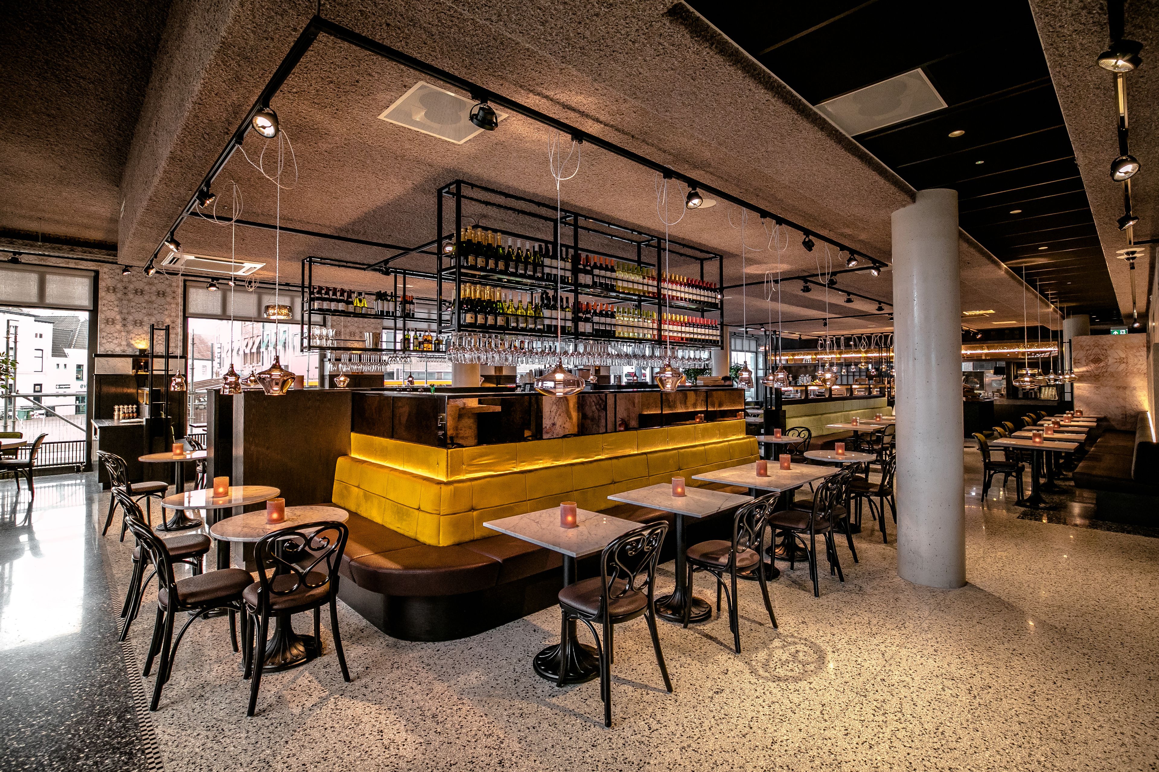 A modern bar area with a central counter, multiple seating tables, and a variety of bottles and glasses on shelves.