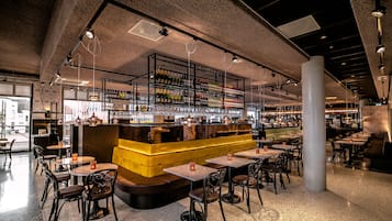 A modern bar area with a central counter, multiple seating tables, and a variety of bottles and glasses on shelves.