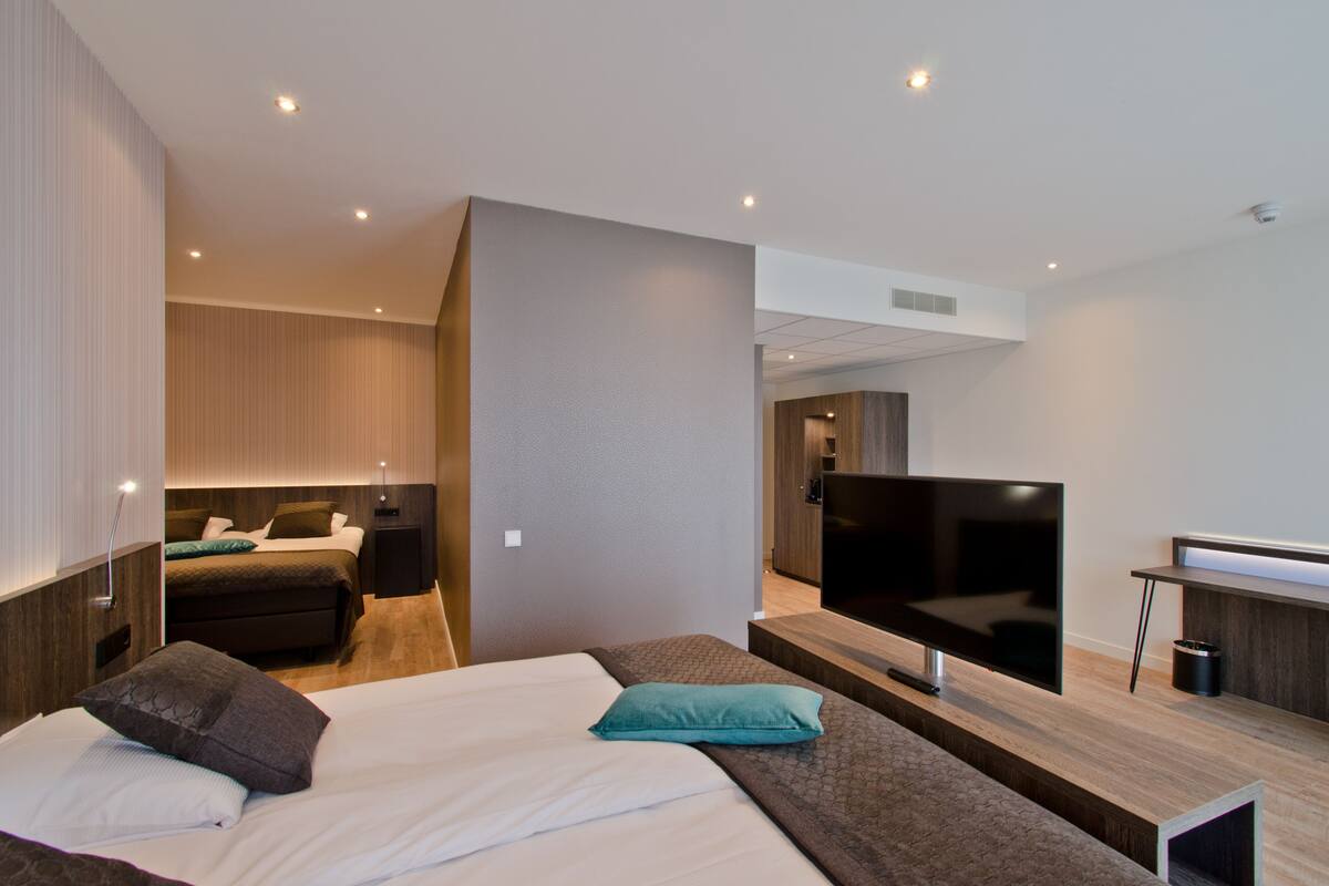 A modern hotel room with a large bed, a TV, a desk, and a separate seating area.
