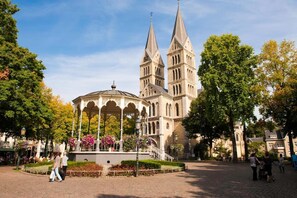 A historic building with two tall spires, a central pavilion, and a paved courtyard.