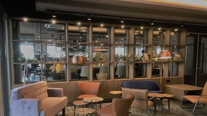 Un área de lounge moderna con asientos acolchados, pequeñas mesas redondas y un ventanal con vistas a la calle.
