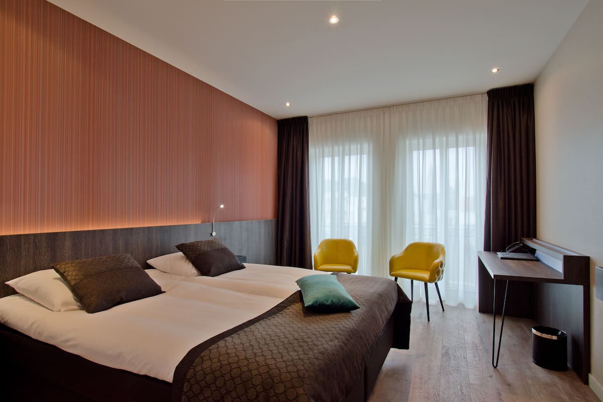 A hotel room with a large bed, two chairs, a desk, and a view of the outdoors through the window.