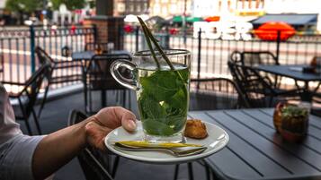 Une personne tenant un verre de thé agrémenté de feuilles de menthe sur une table, dans un cadre extérieur.