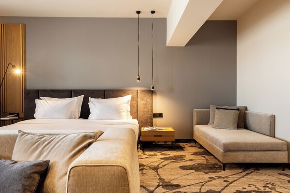 Una habitación de hotel moderna con una cama grande, un sofá, una mesita de noche y una lámpara.