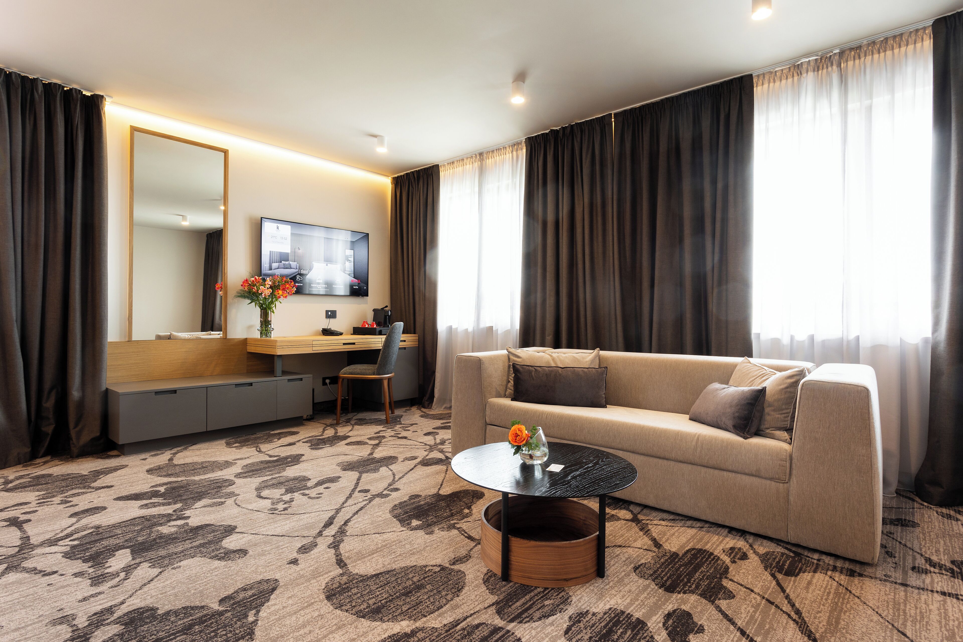 Una habitación de hotel moderna con sofá, una mesa de centro, televisor y escritorio con silla.