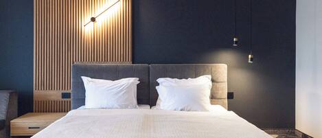 A modern hotel room with a large bed, two white pillows, a wooden accent wall, and a wall-mounted light fixture.