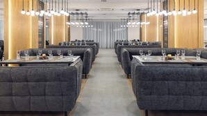Un ristorante moderno con sedute e tavoli rivestiti in grigio, ognuno apparecchiato con bicchieri da vino e bicchieri d'acqua.
