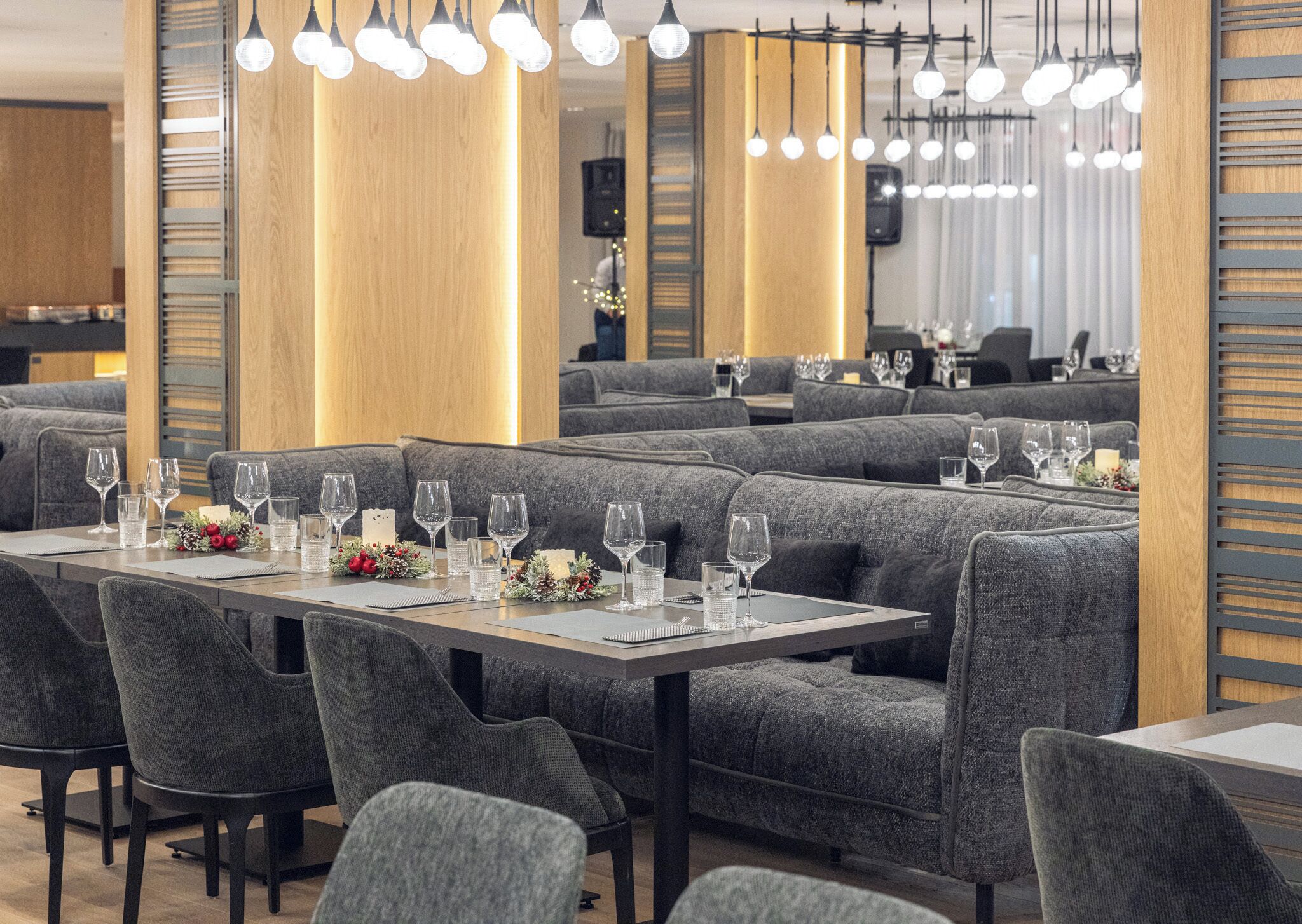 En moderne restaurant med grå polstrede bænke, pænt anrettede borde med vinglas og hængende lamper.