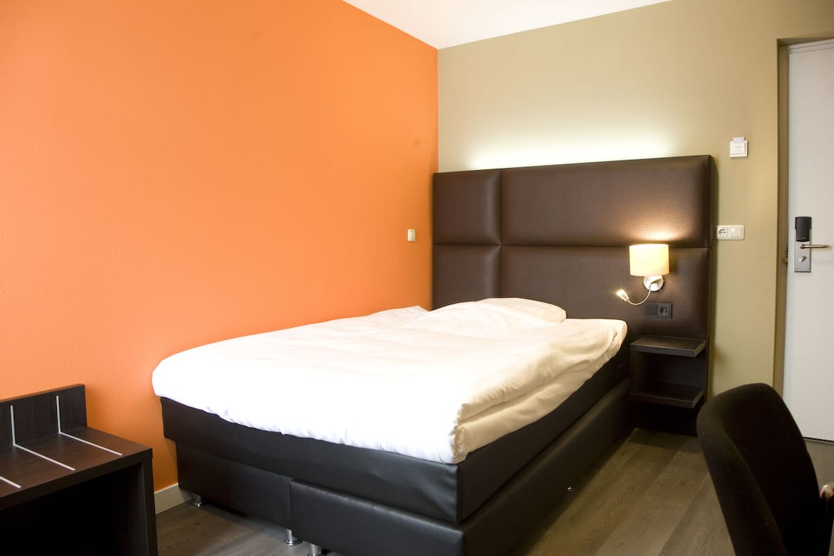 Una habitación de hotel con una cama, una mesita de noche, un escritorio y una silla.