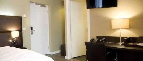 A hotel room with a bed, desk, chair, TV, and lamp.