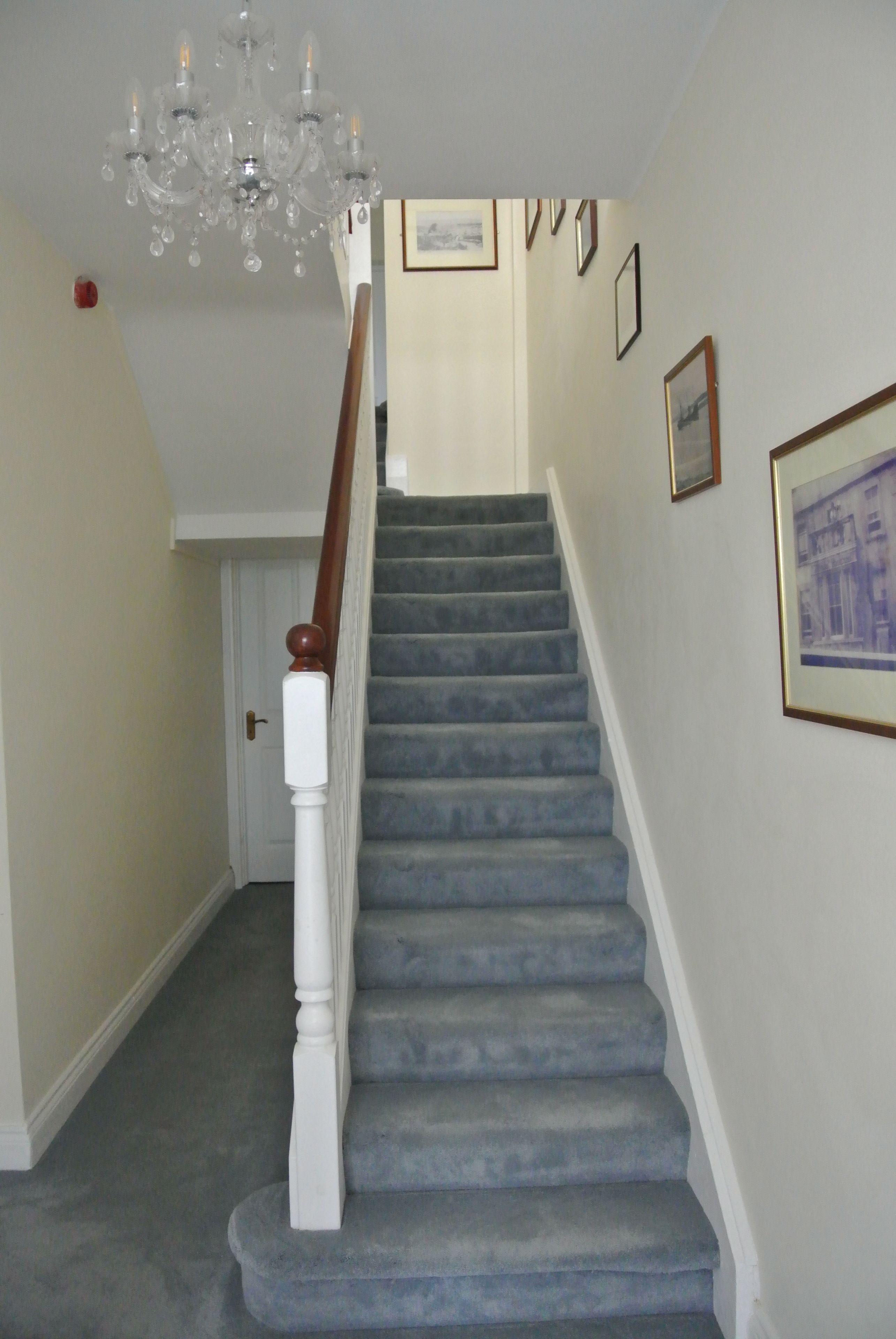 A staircase with a wooden handrail and a chandelier.