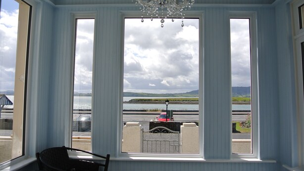 A room with a large window offering a view of a body of water and distant landscape. - Sligo Bay Lodge (Rosses Point)