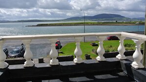 A balcony with a view of a body of water, a grassy area, and a distant mountain range. - Sligo Bay Lodge (Rosses Point)