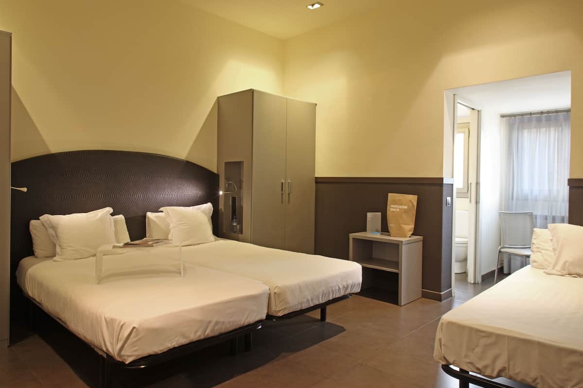 Habitación de hotel con dos camas, un armario, una mesita y un baño visible a través de una puerta abierta.